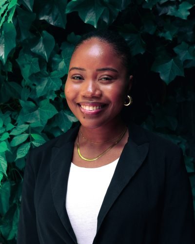 Jeune femme souriante en tenue professionnelle devant un mur végétal, représentant l’accueil client chaleureux et soigné d’Indifair.