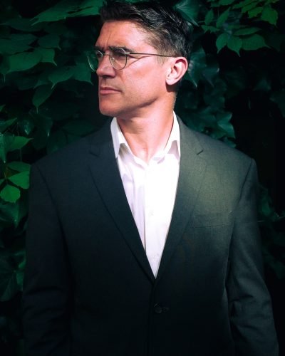 Homme en costume regardant sur le côté, dans un décor végétal, incarnant l’élégance et l’exigence professionnelle d’Indifair.